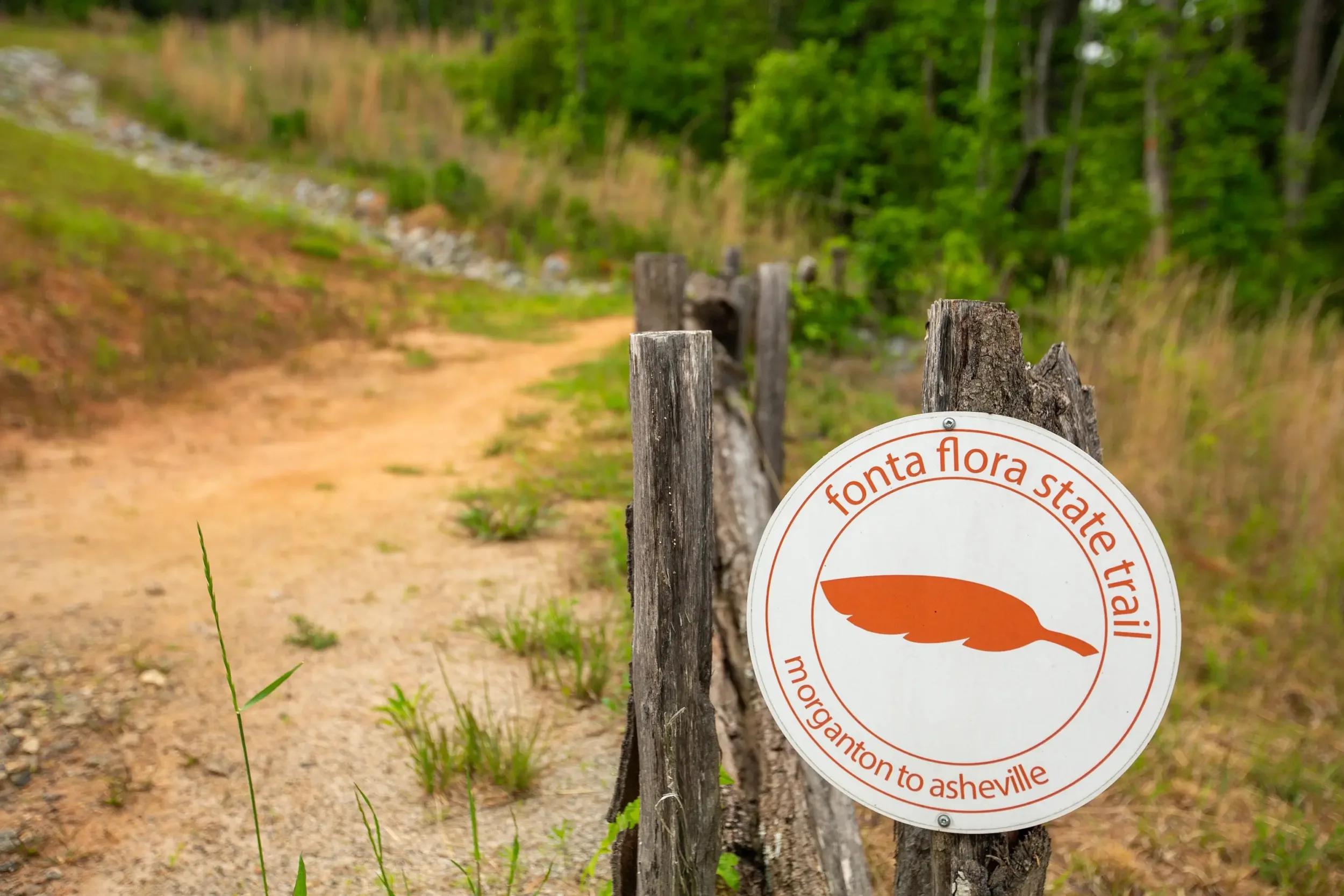 A round Fonta Flora State Trail sign denoting that it leads from Morganton to Asheville