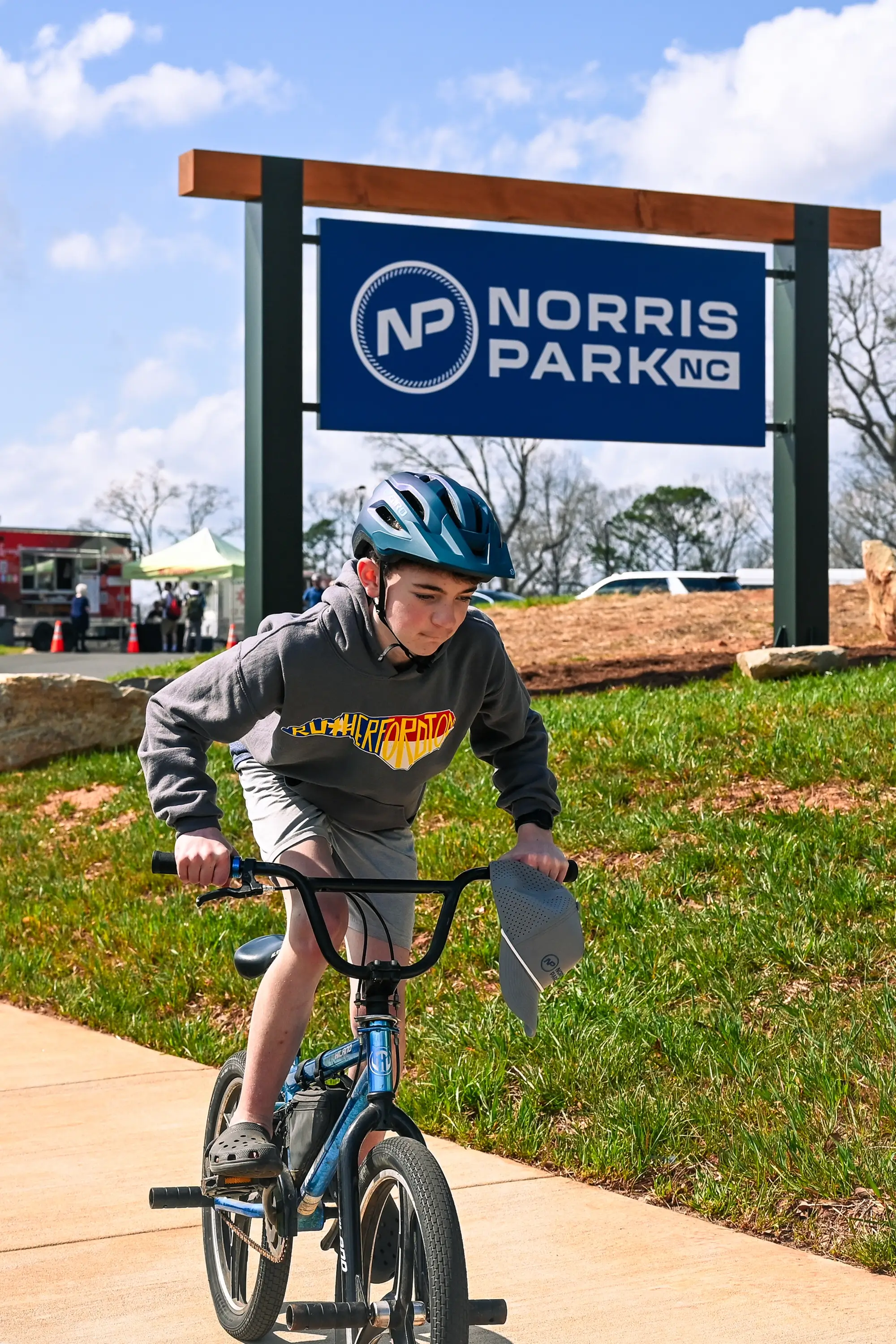 A kid riding his bike past the Norris Park entrance sign