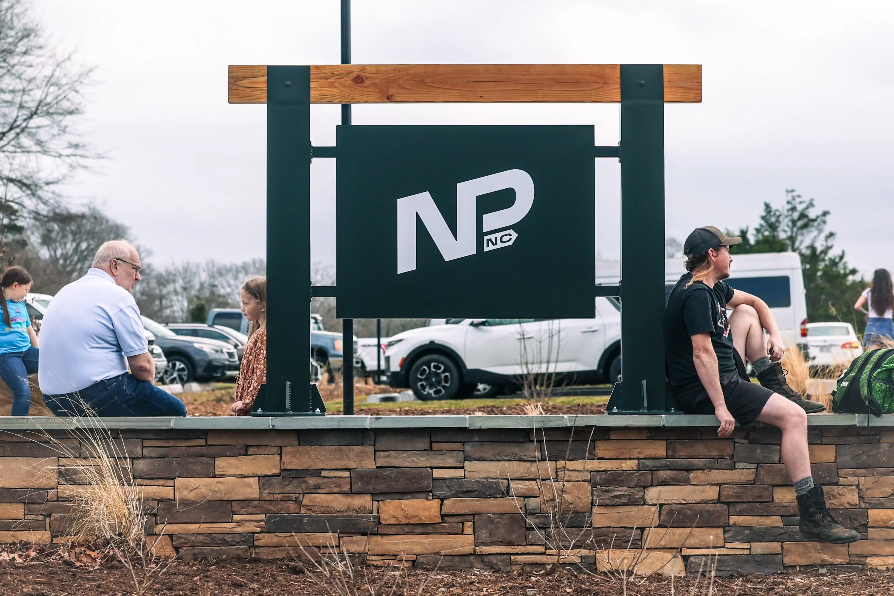 Visitors sitting on the rock wall by the Norris Park signage