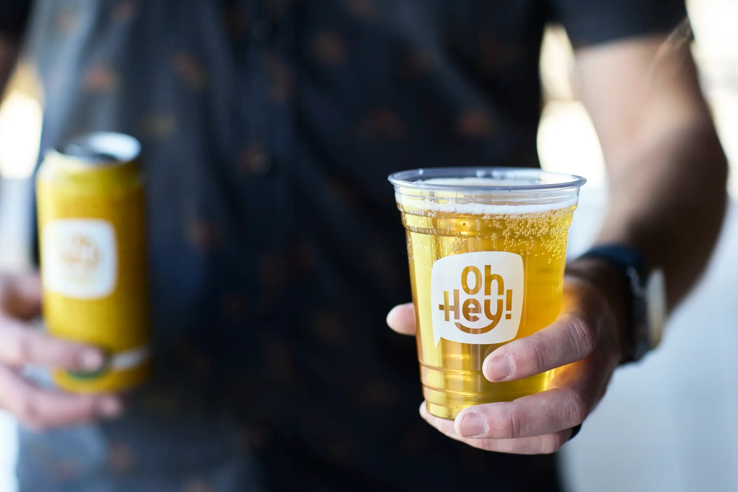 A man holding a plastic cup that has the "Oh Hey!" mark printed