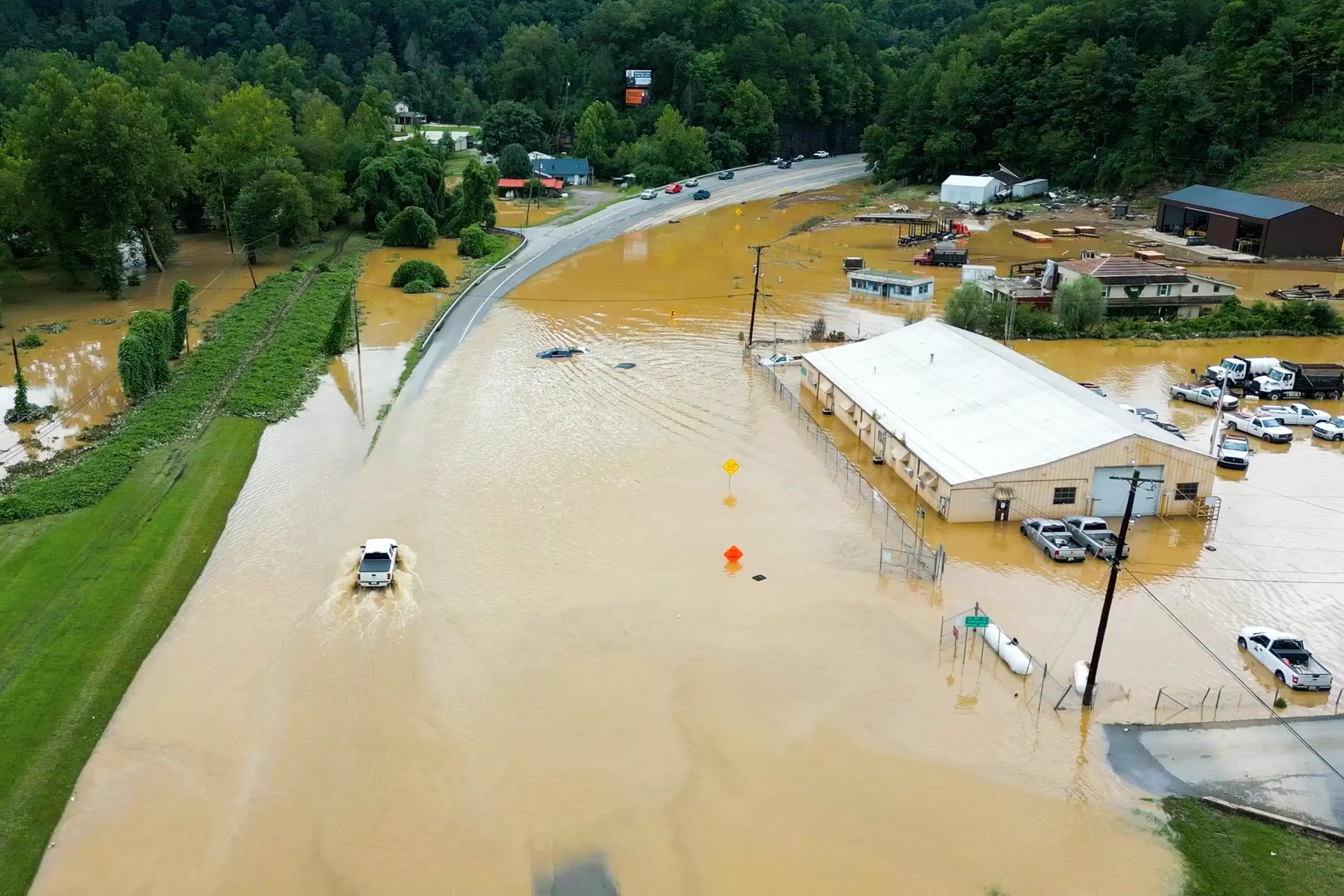 A truck driving on a flooded road next to businesses in water