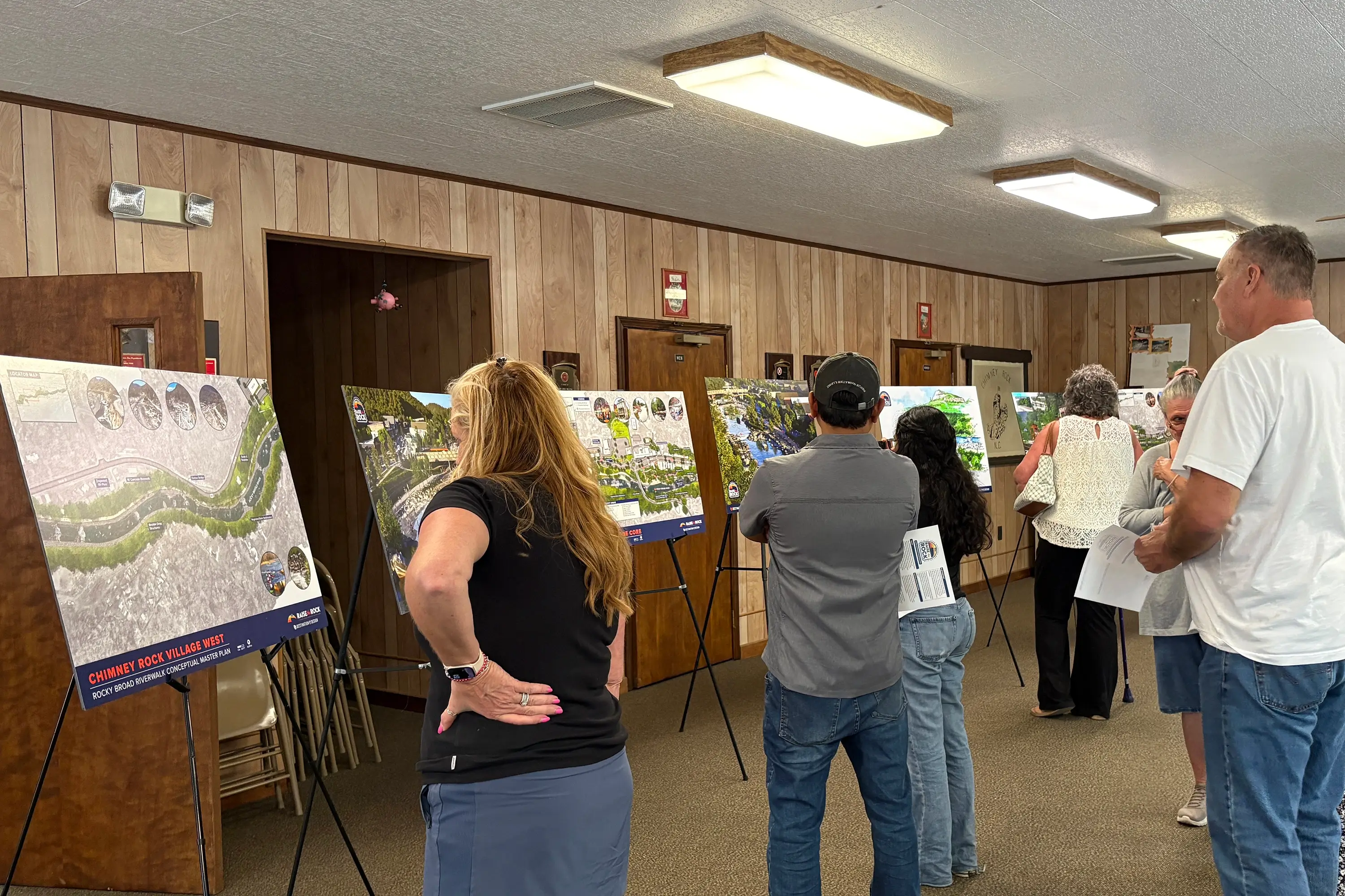 A group gathered looking at various boards of renders and plans