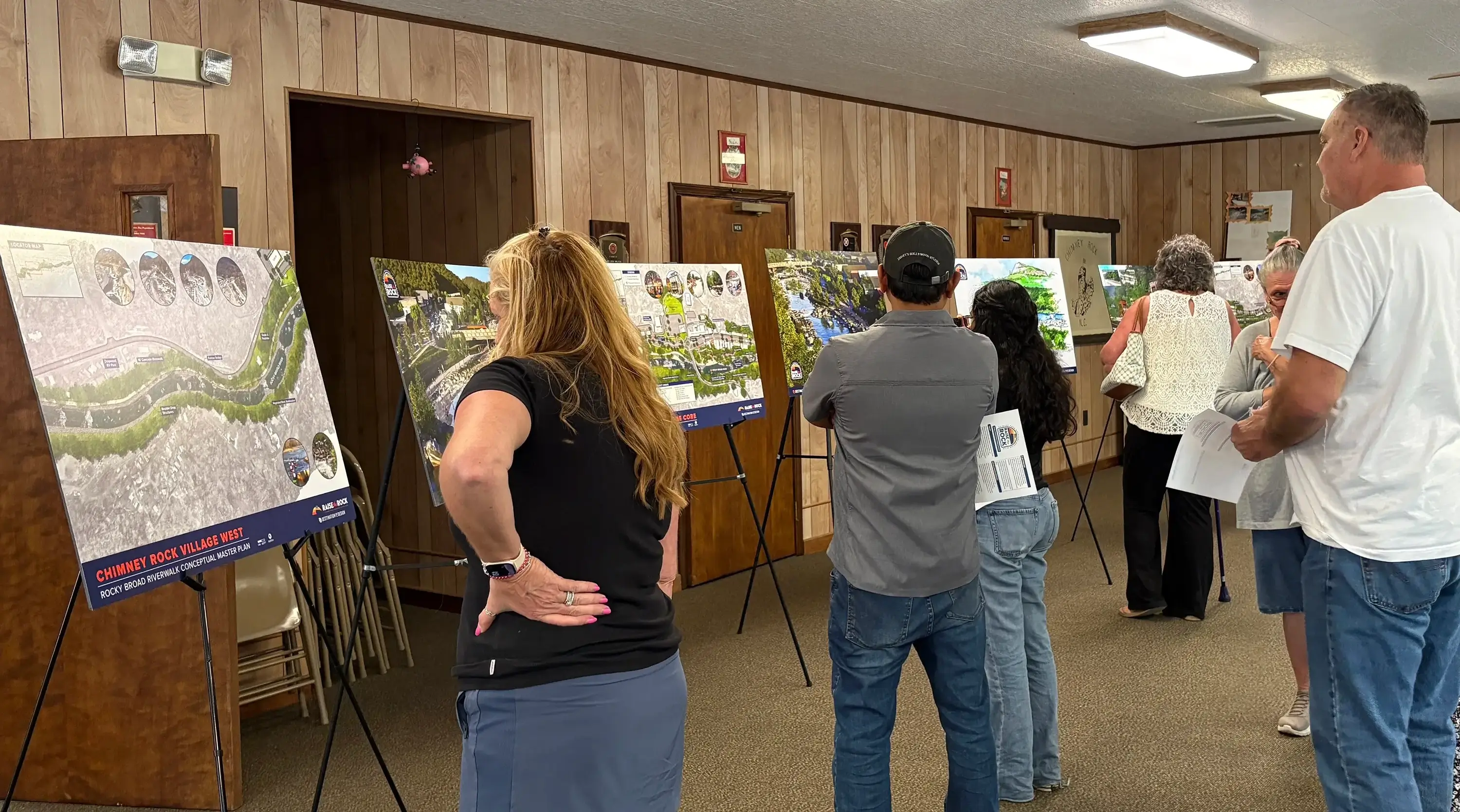 A group gathered looking at various boards of renders and plans