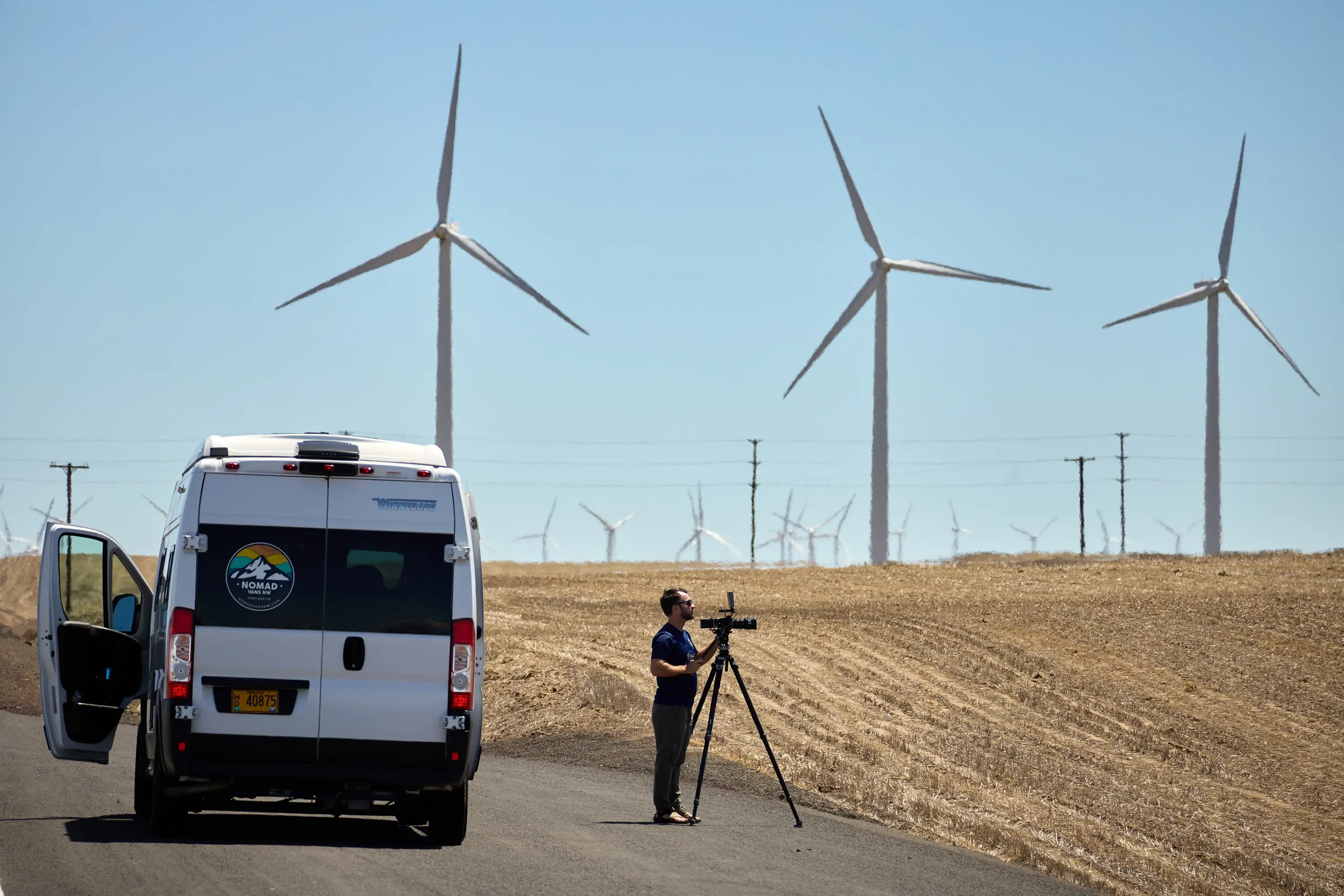A videographer standing on the road with windmills in the background